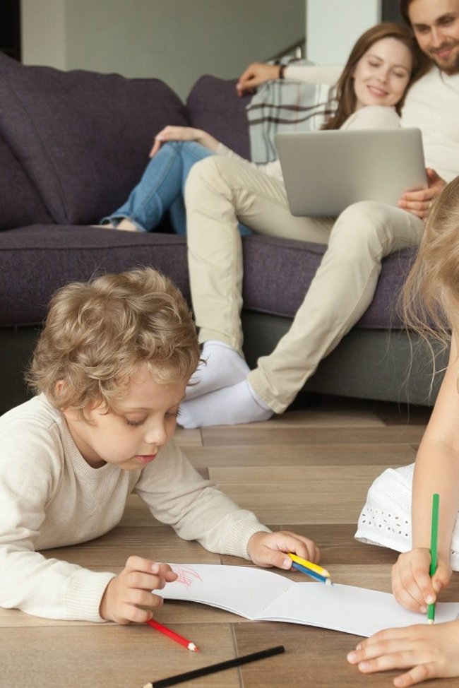 Paar sitzt auf Couch während Kinder am Boden sitzen und Malen.