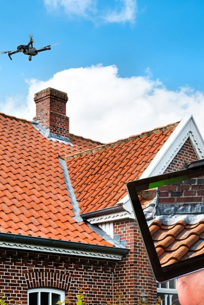 Haus über dem eine Drohne schwebt. Auf einem Bildschirm sieht der Schadensachverständige die Bilder von der Drohne.