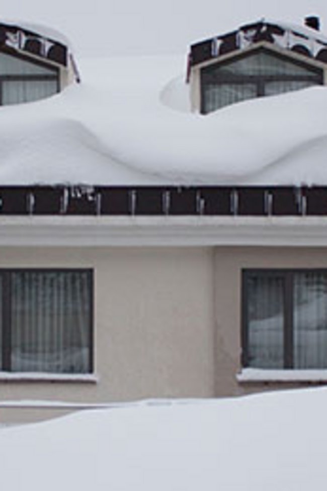 1038007819 Haus stark von Schnee bedeckt, Dach und Umgebung tief verschneit.