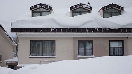Haus stark von Schnee bedeckt, Dach und Umgebung tief verschneit.