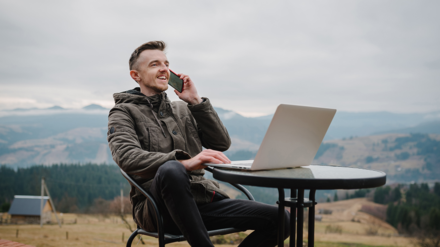 Digitalisierung. Mann mit Laptop und Handy sitz auf Berg und arbeitet