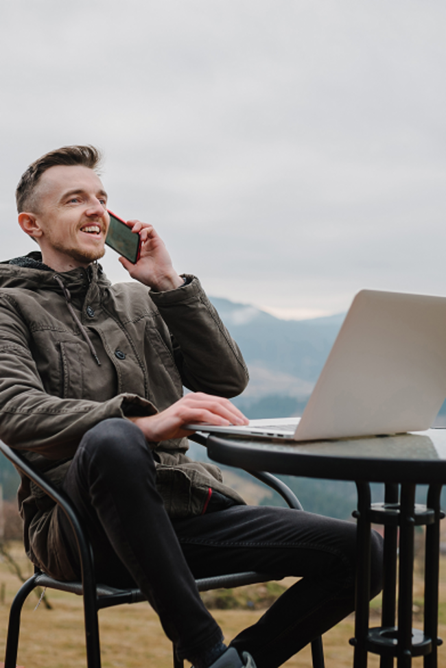 Digitalisierung. Mann mit Laptop und Handy sitz auf Berg und arbeitet