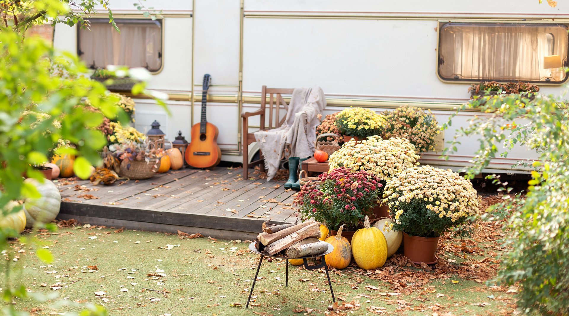 Herbstlich dekorierter Gartentisch mit Stühlen vor einem Wohnwagen.